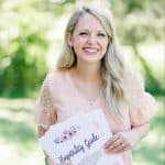 Brettnay Brazzell smiling in her peach colored dress while holding "The Hospitality Guide." There are trees and grass in the background out of focus.