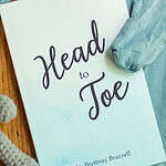 The Blue edition of the Head-to-Toe Prayer Journal. It is laying on a set of blue baby pajamas with a grey knitted teddy bear next to it.