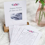 labor and delivery cards. It depicts the front card in a wooden stand with other cards flayed out in front of it. They are laying on a white blanket with a small vase of pink flowers beside them.