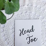 Head to Toe Prayer Journal. The white edition of the book is laying on a white tablecloth with a green plant next to it.