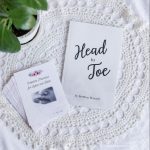 A white Head-to-Toe Prayer journal and the "Scripture Promises for Labor and Birth" cards laying on a white blanket with a green plant next to them.