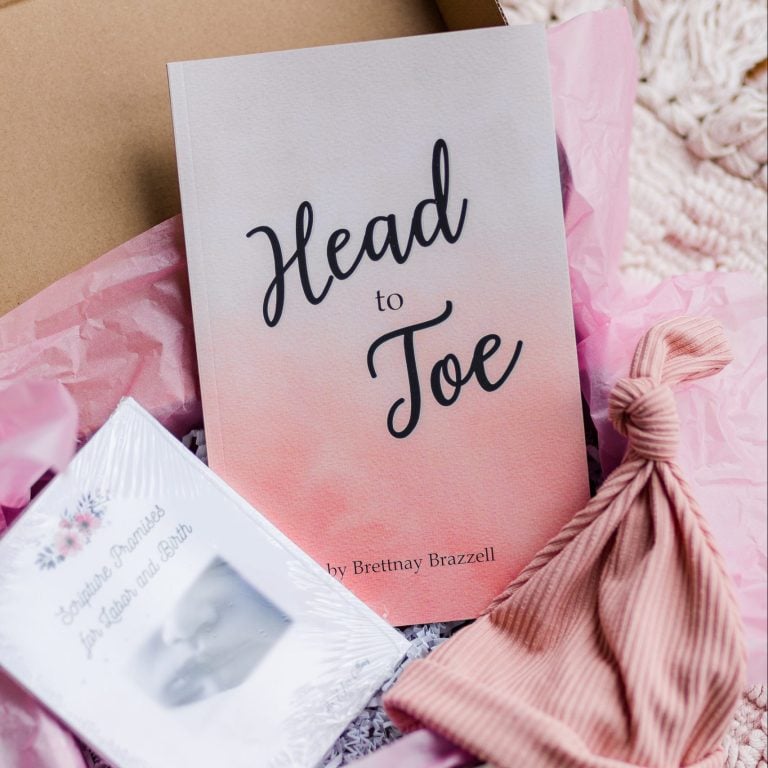 A close up of the pink box set. It has the three products in a brown box one a white blanket. Includes a Head-to-Toe Prayer Journal, the Scripture Promises Labor and Birth Cards, and a baby hat