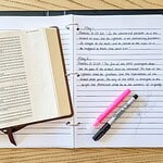 Open notebook with scripture written under daily headings shown with an open Bible, a highlighter, and a pen