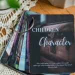 Image of the "Children of Character Cards" flayed out on a table. The front card shows the title with a treasure chest on it. On the table are the cards, a candle, and a plant.