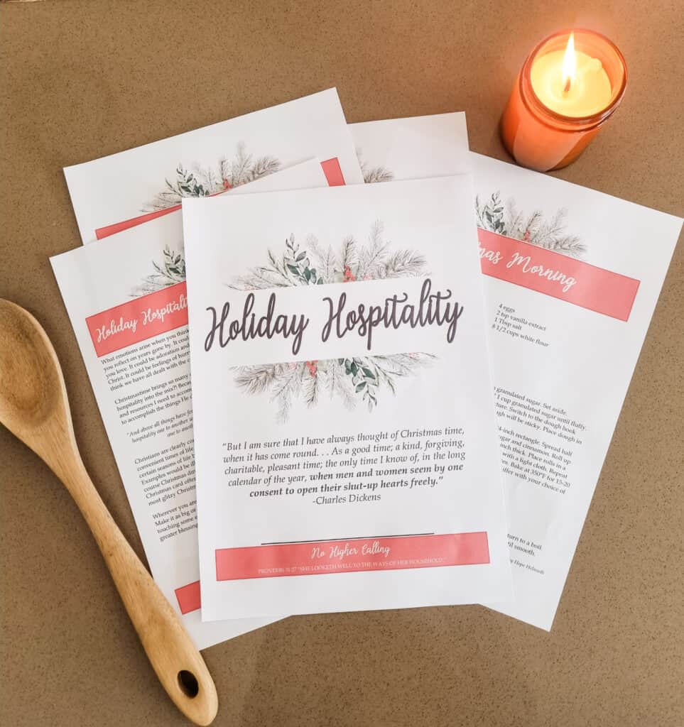 The Holiday Hospitality Guide laying out on a brown background. Next to it are a candle which is lit and a wooden spoon.