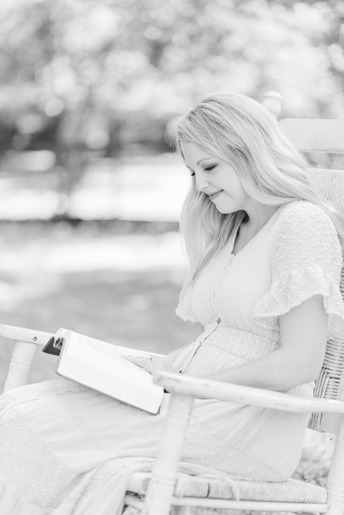 A black and white image of Brettnay Brazzell sitting on a rocking chair with her Bible in her lap. In the background are grass and trees blurred out of focus.