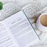 Great Hymns for Growing Hearts Interior Image showing the music to the hymn along side the story behind the hymn. The book sits on a table with hot chocolate and a plant.