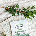 Great Hymns for Growing Hearts book laying on a table with flowers around it. On the table is a hymn book laying open as well.