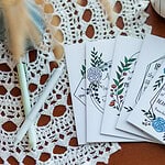 Five Friendship Cards flayed out on a wooden table that is covered in lace with 2 pens beside them.