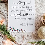 A single Christmas card laying on white fir and surrounded by greenery. It reads "Glory to God in the highest, and on earth Peace, good will towards men." Luke 2:14