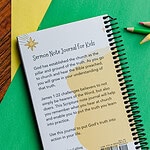 The back side of the sermon note journal showing the descriptive text. It is laying on green and yellow paper with colored pencils