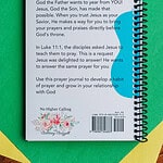 The Teach Me To Pray Prayer Journal laying on a piece of green and yellow construction paper on top of a table. There are colored pencils beside it. It shows the back of the journal with the description.